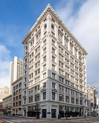 A tall, historic white commercial building with ornate architectural details on a city street corner under a blue sky.