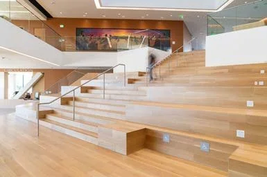 Modern indoor staircase with wooden steps and glass railing in a spacious building.
