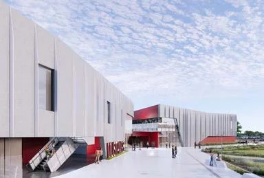 Modern building with white exterior, red accents, and an open entrance, surrounded by a walkway under a partly cloudy sky.