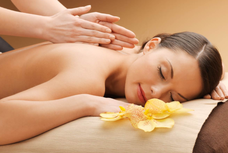 A woman receiving a back massage in a spa setting with yellow flowers on a massage table.