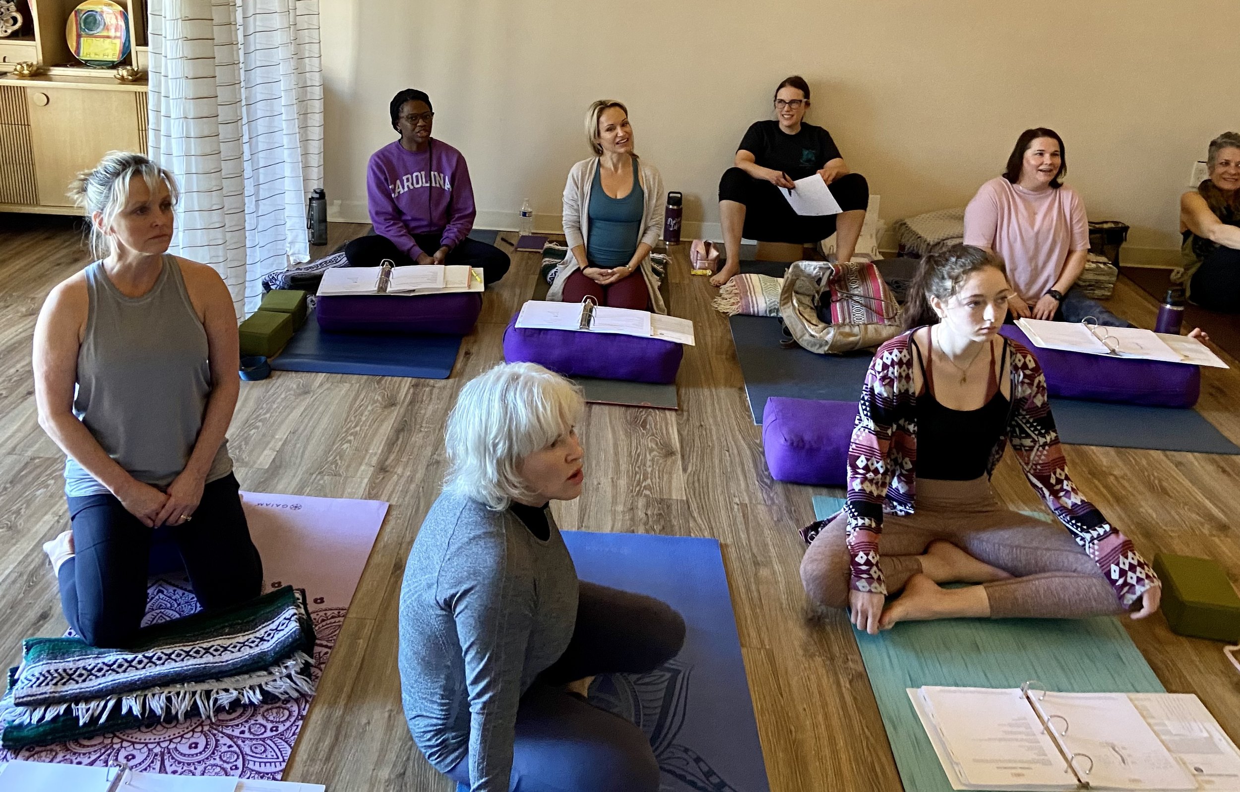 Students of Pamela sit cross-legged on the floor taking notes in their yoga teacher training binders.