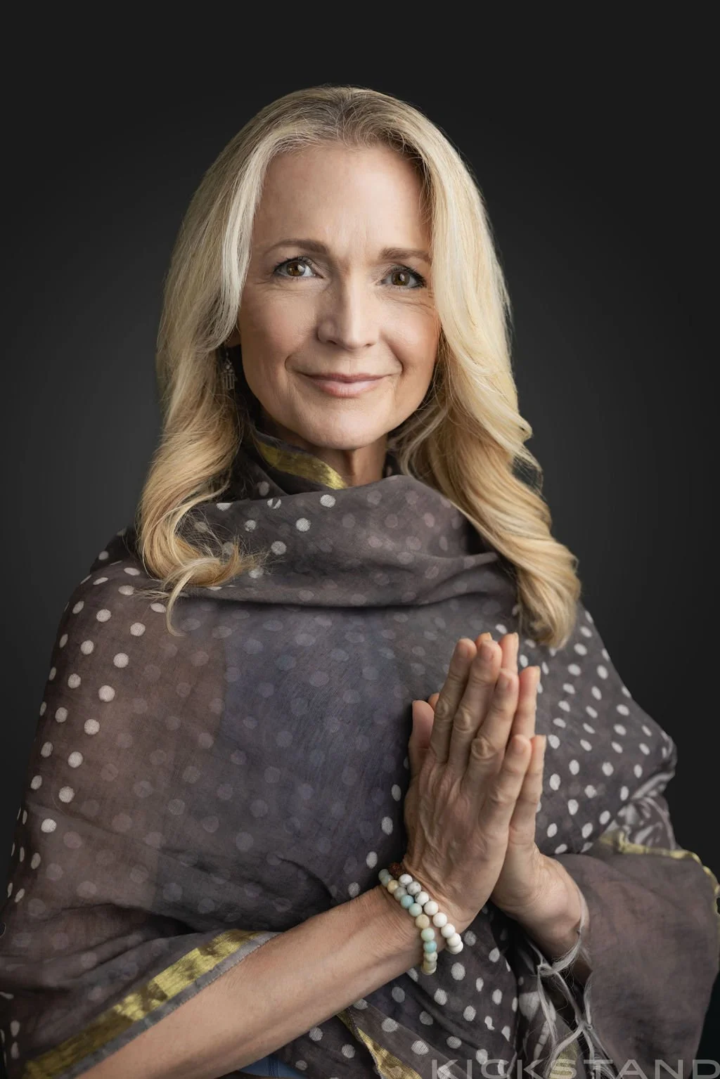 Pamela wrapped in a dark colored sari with gold details with her hands in prayer pose.
