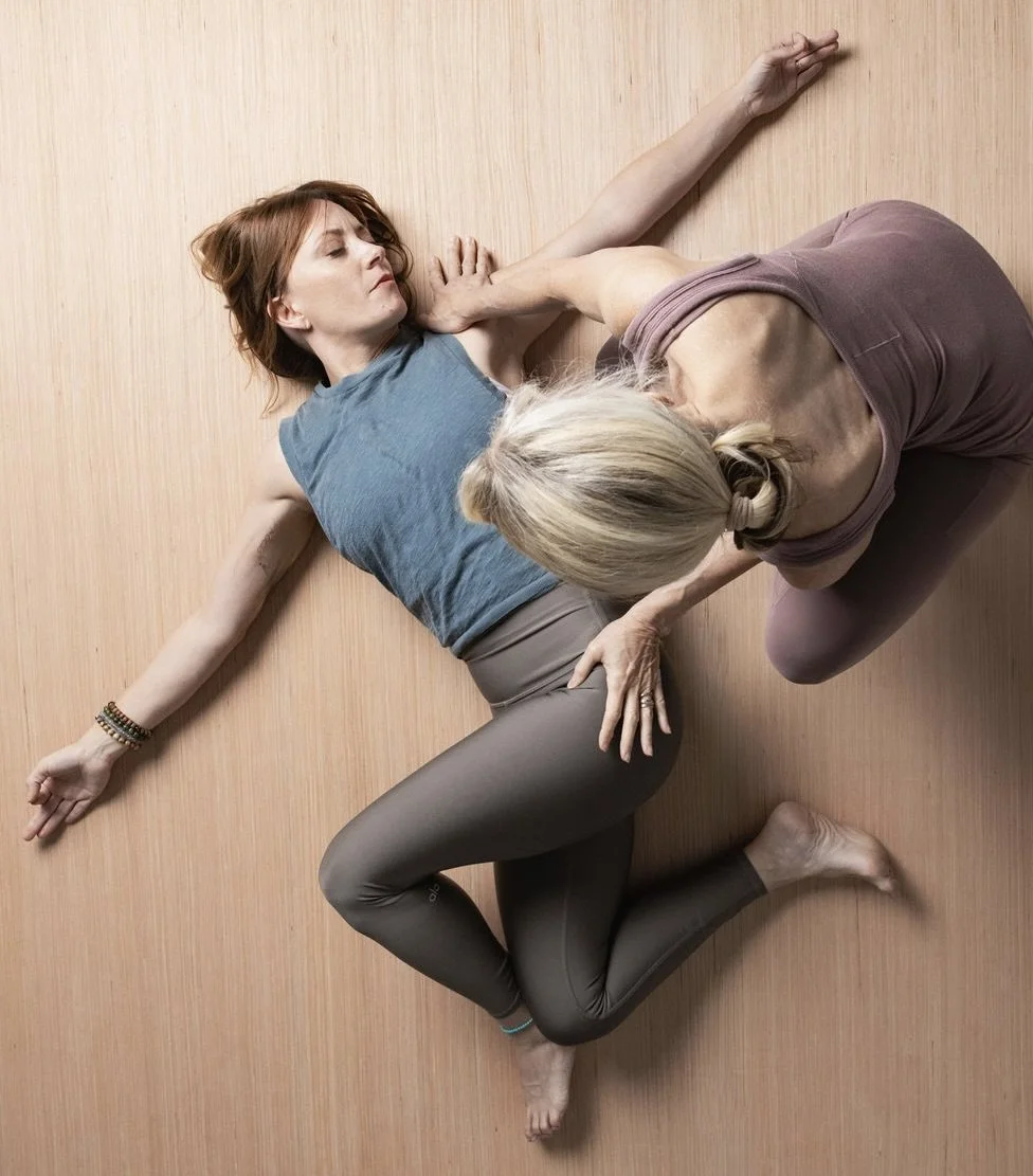 Pamela Meriwether gently adjusts a yoga practitioner in a prone twist.