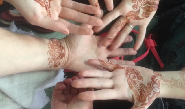 Multiple hands displaying henna designs on their palms and wrists.