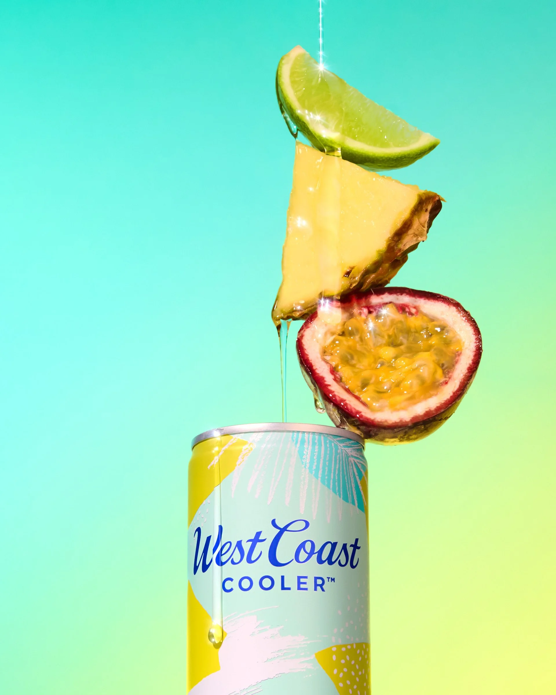 A tall can of West Coast Cooler with colorful fruit slices, including lime, pineapple, passion fruit, and strawberry, stacked on top of each other against a gradient turquoise background.
