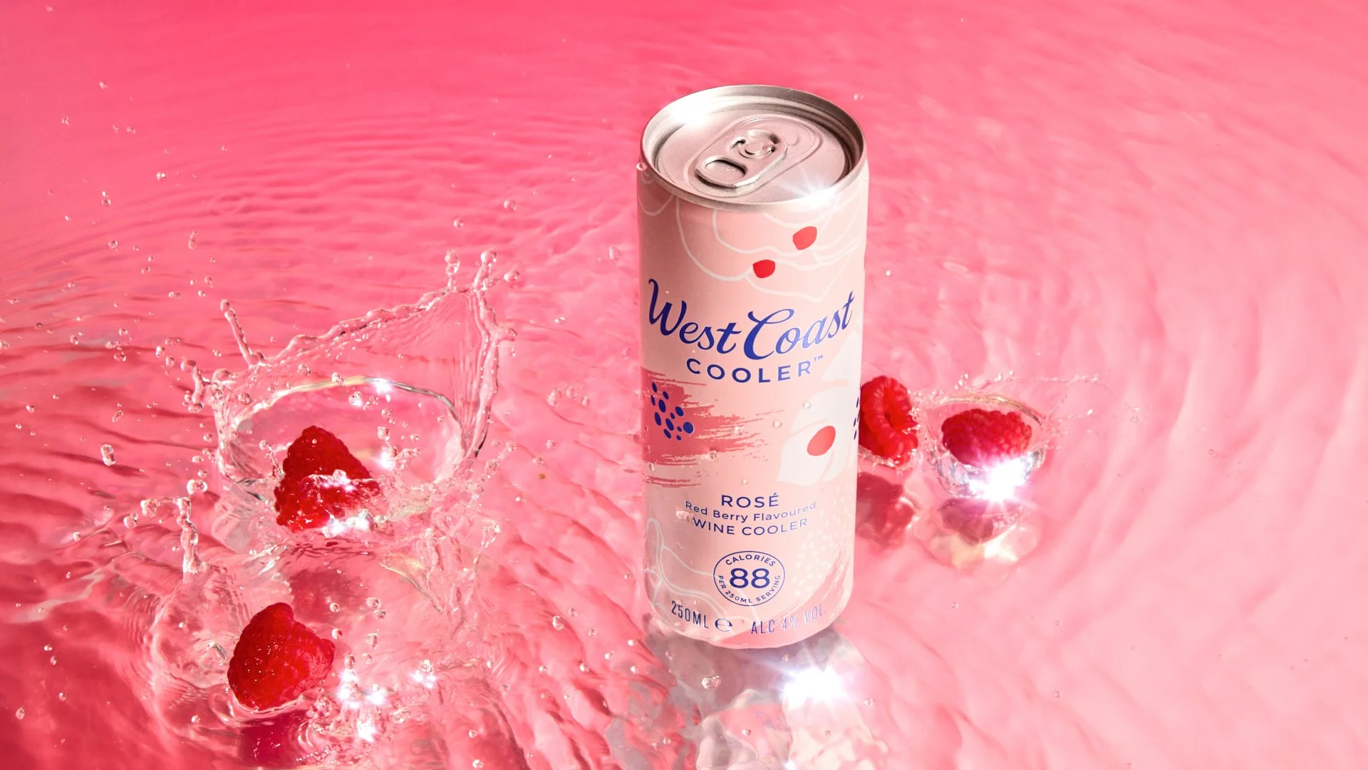 A can of West Coast Cooler rosé wine cooler submerged in pink water with raspberries, creating splashes and bubbles.