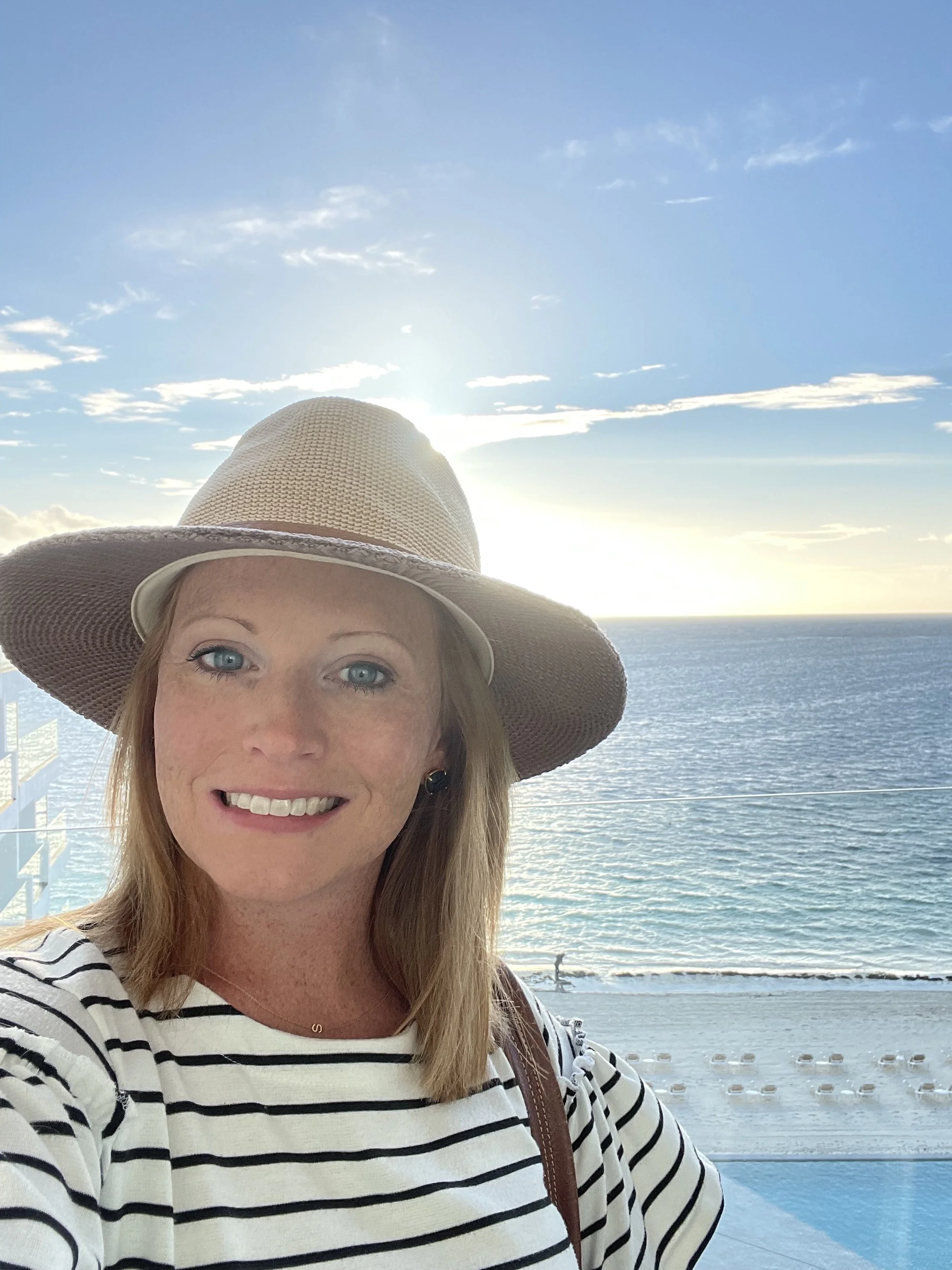 Travel agent, Samantha Harris, smiling in front of the ocean during sunset or sunrise.