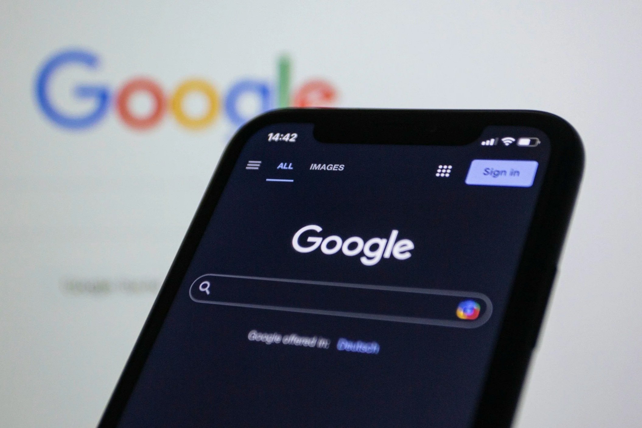 Close-up of a smartphone screen browsing Google with a blurred Google logo in the background.