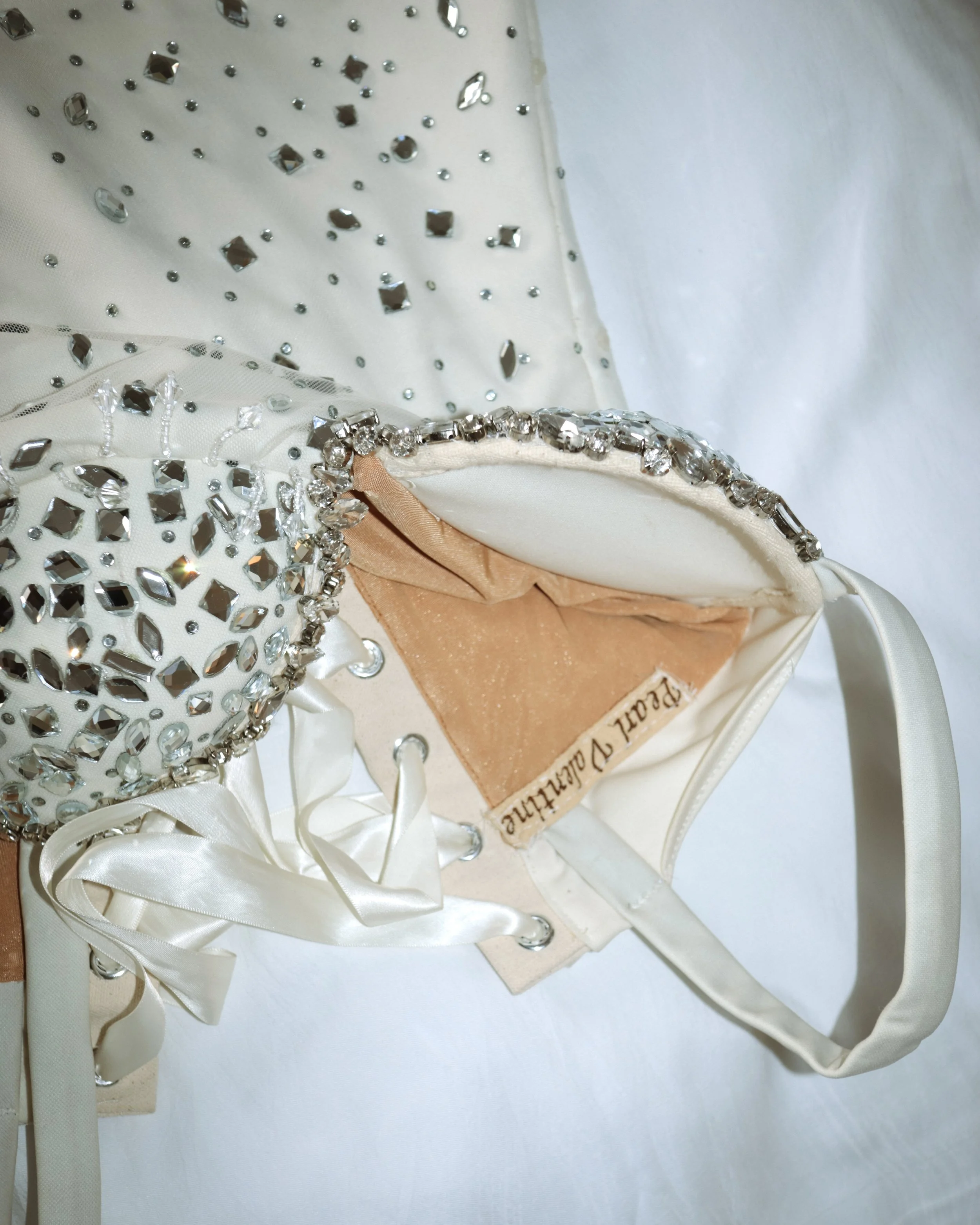 A white handbag with rhinestone embellishments on the strap, partially open to reveal a peach-colored interior lining with a "Peach Parfait" label inside.