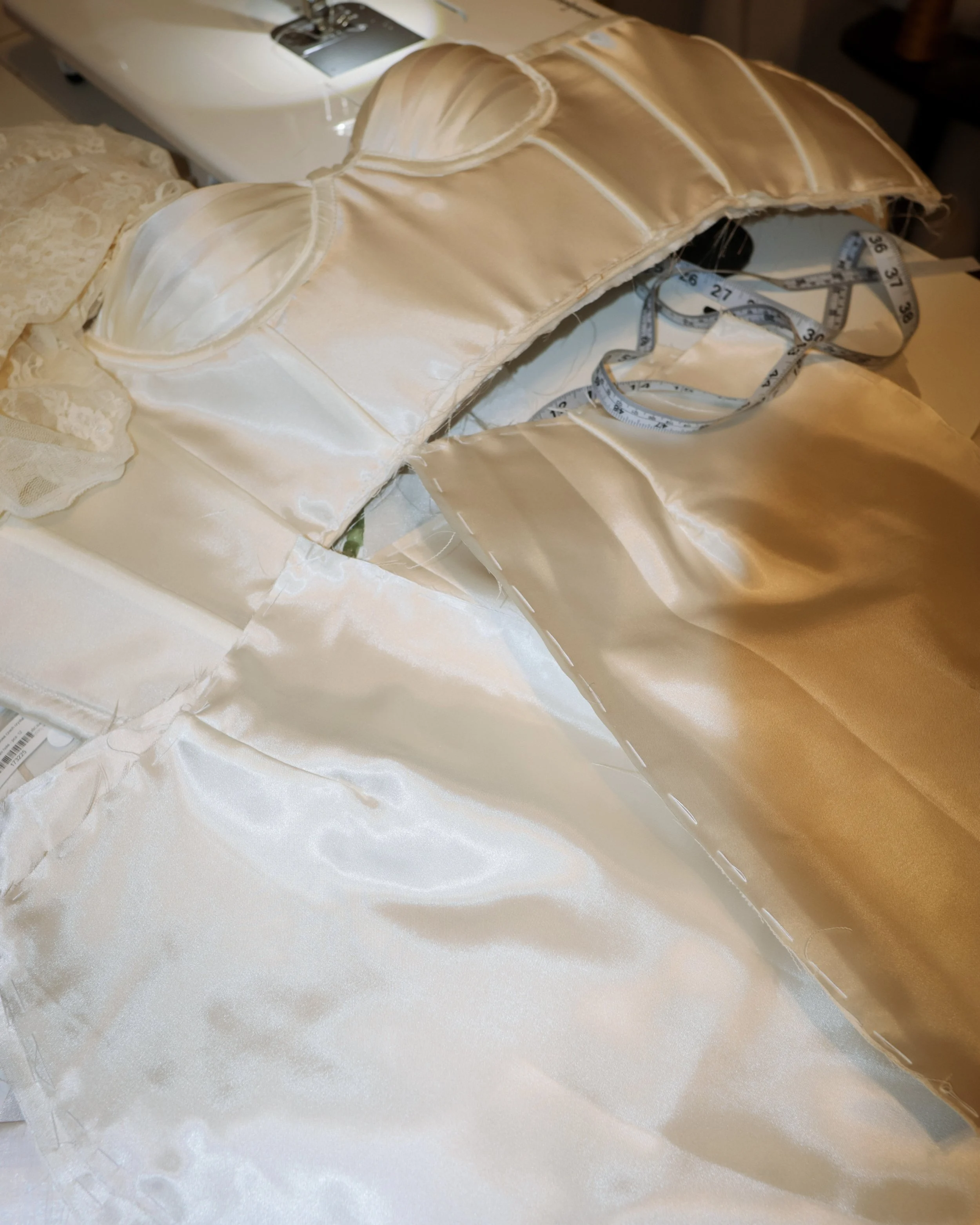 A silk or satin fabric for a wedding dress, featuring a built-in bra with padded cups, lying on a table with a measuring tape nearby.