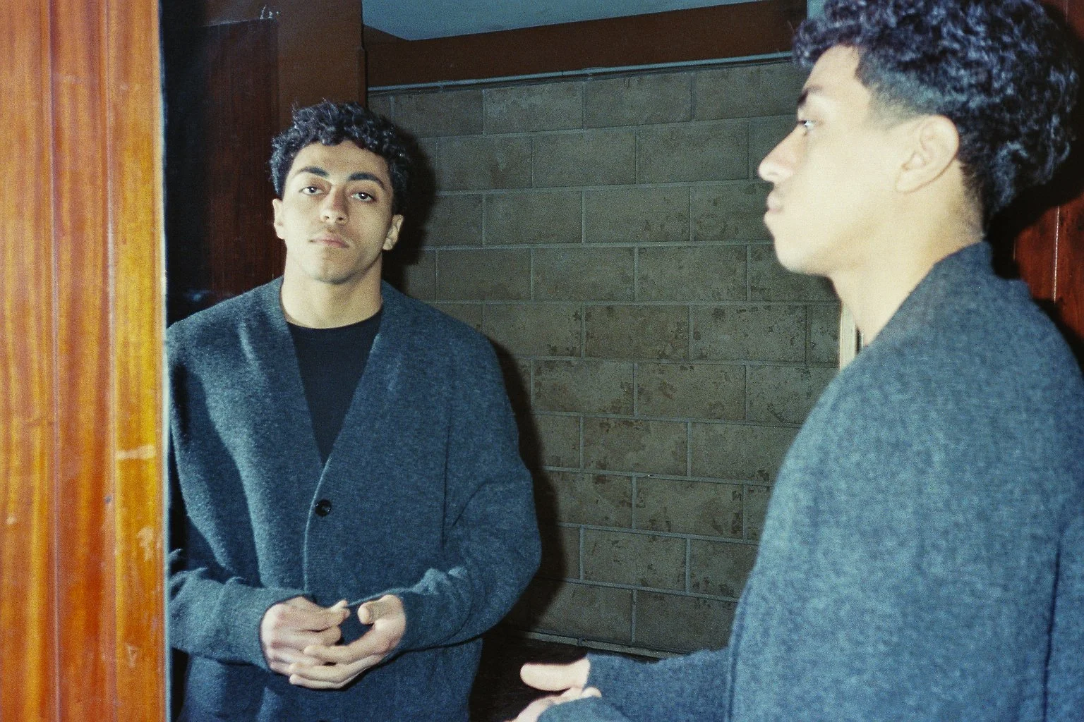 Ragazzo in front of uno specchio, visto di profilo, con la mano in tasca, mentre guarda il suo riflesso in modo serio.