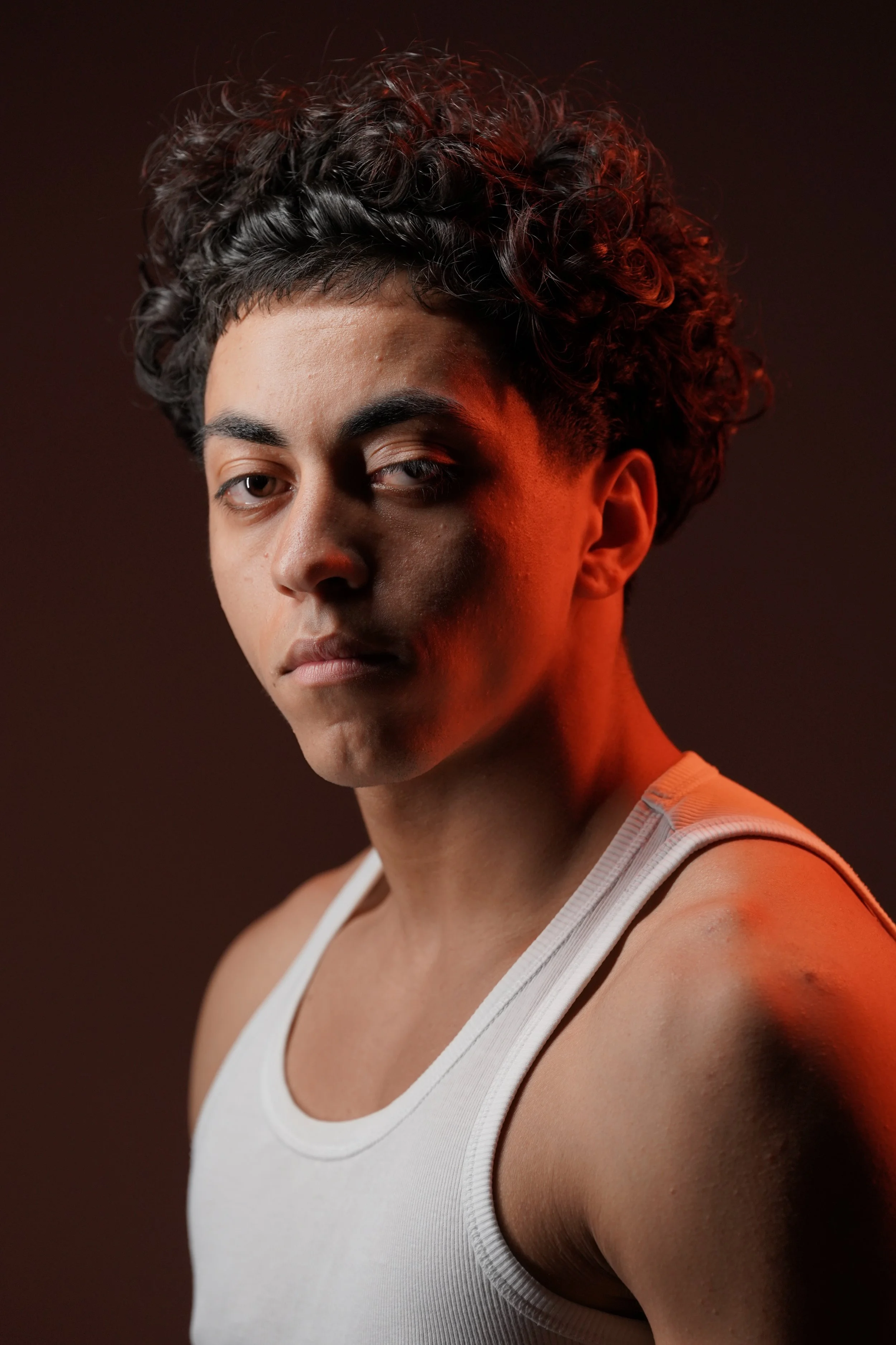 Ritratto di una giovane donna con capelli ricci, abbigliamento sportivo bianco, sfondo scuro con luci calde.