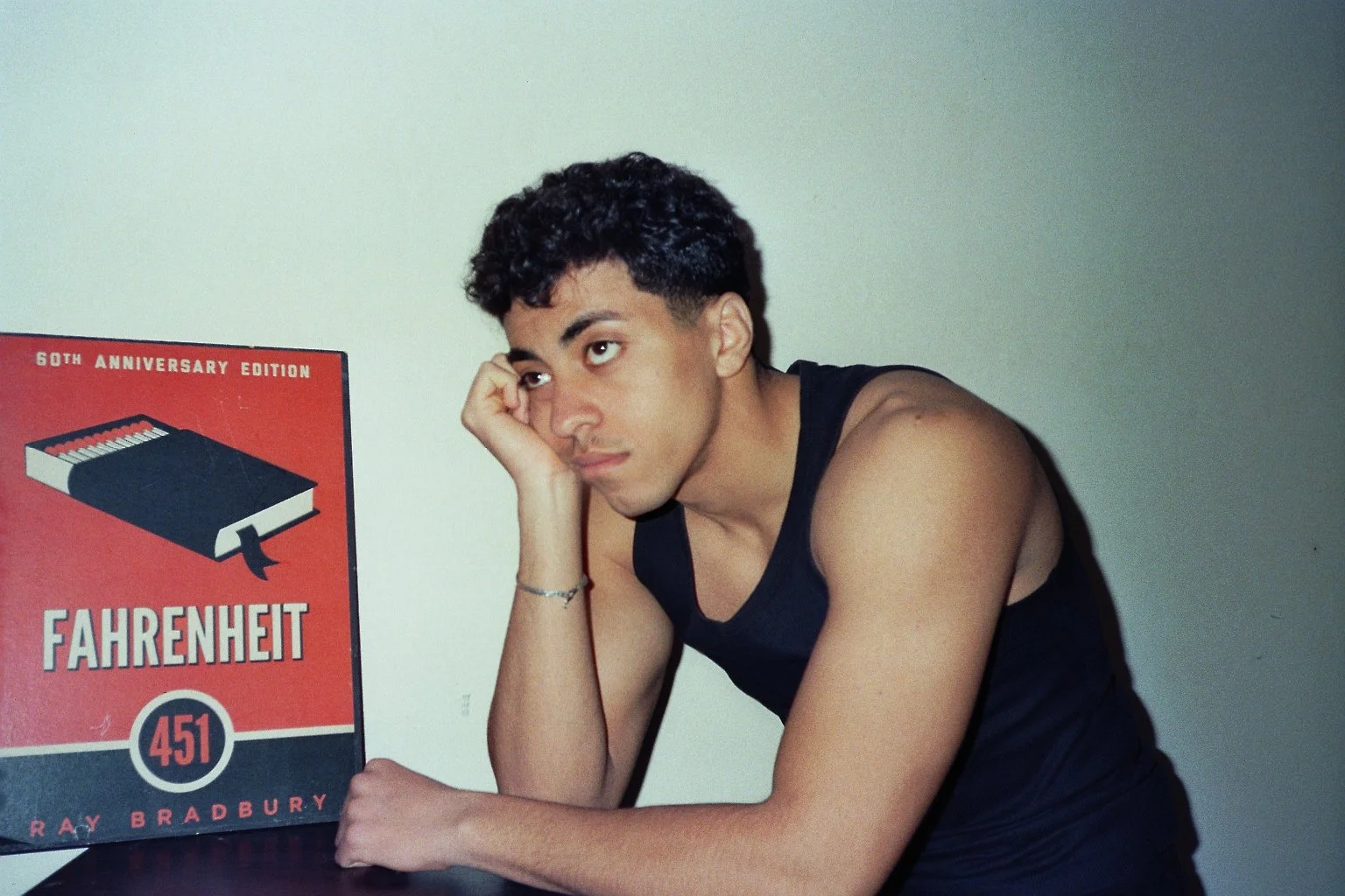 Ragazzo triste con maglietta nera, che si appoggia alla mano, seduto accanto a una copia del libro 'Fahrenheit 451' di Ray Bradbury.