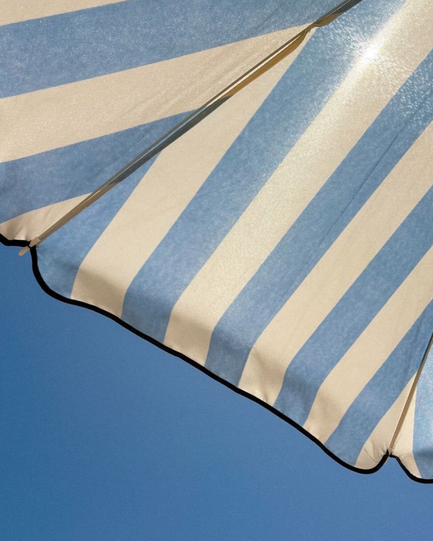 Close-up of a blue and white striped beach umbrella against a blue sky.
