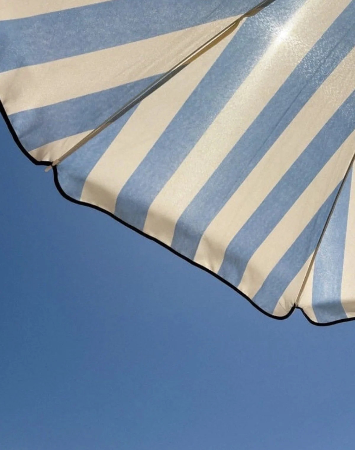 Blue and white striped beach umbrella against a clear blue sky.