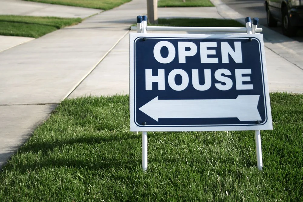 A sign on a grassy lawn indicates an open house event with an arrow pointing to the left.