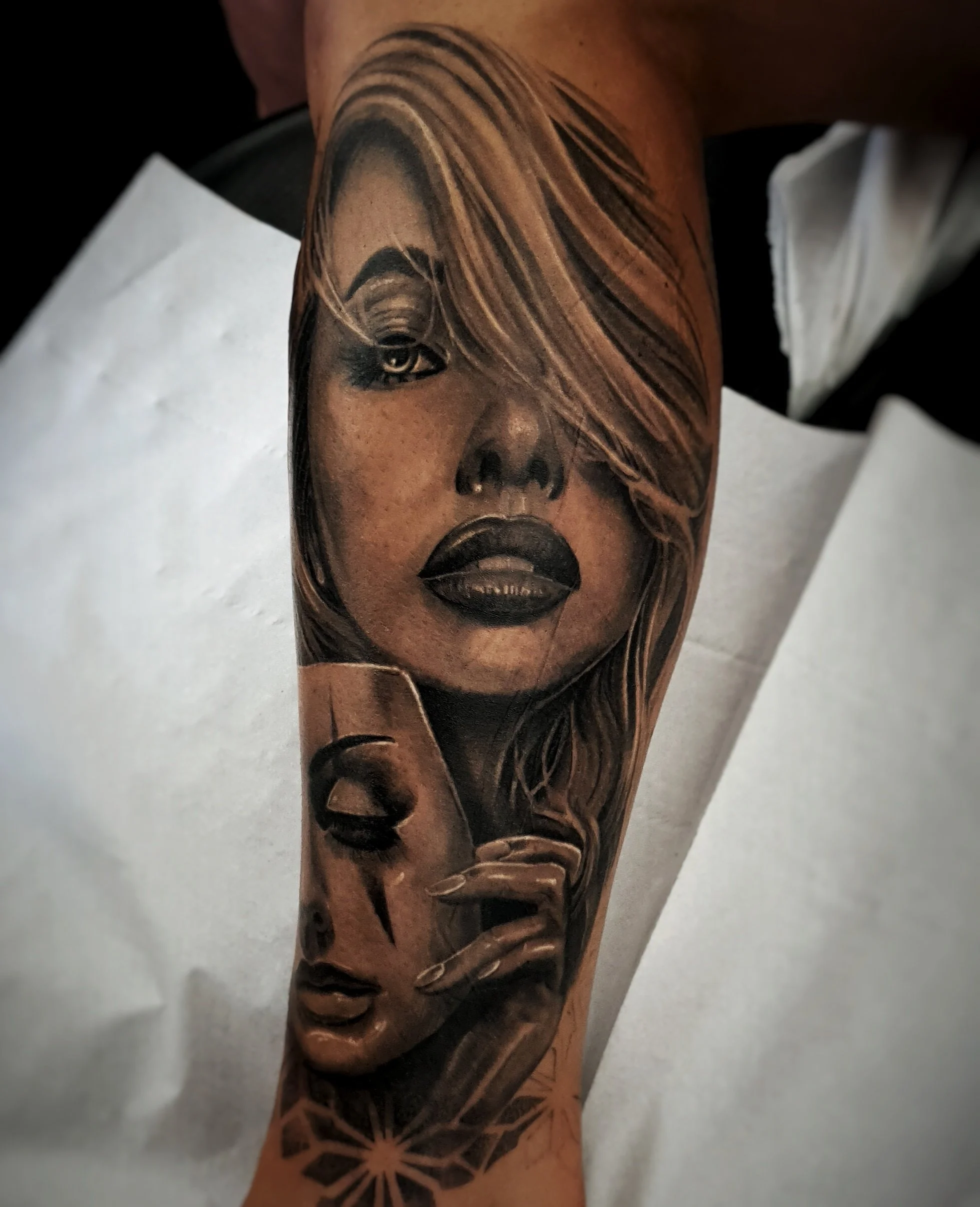 Close-up of a tattoo on a person's arm featuring a portrait of a woman with stylized hair, lips, and eye makeup, with decorative geometric patterns underneath.
