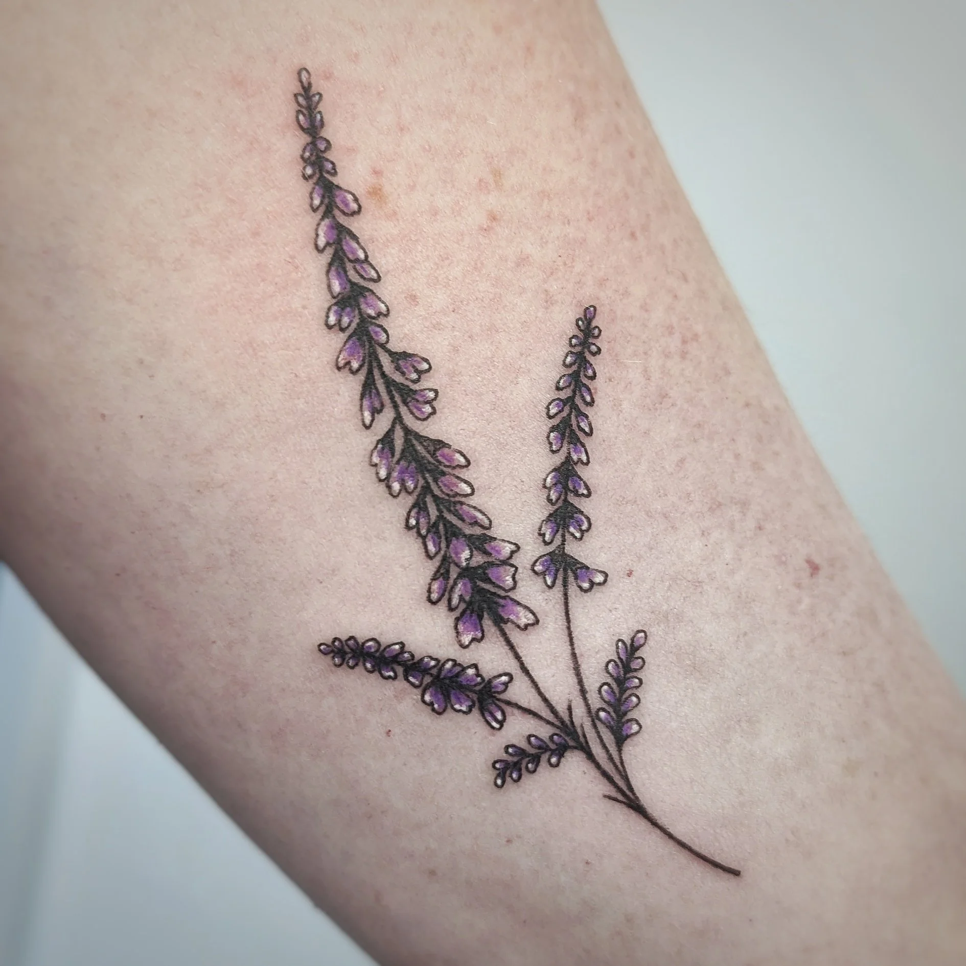 Close-up of a lavender flower tattoo with purple accents on skin.