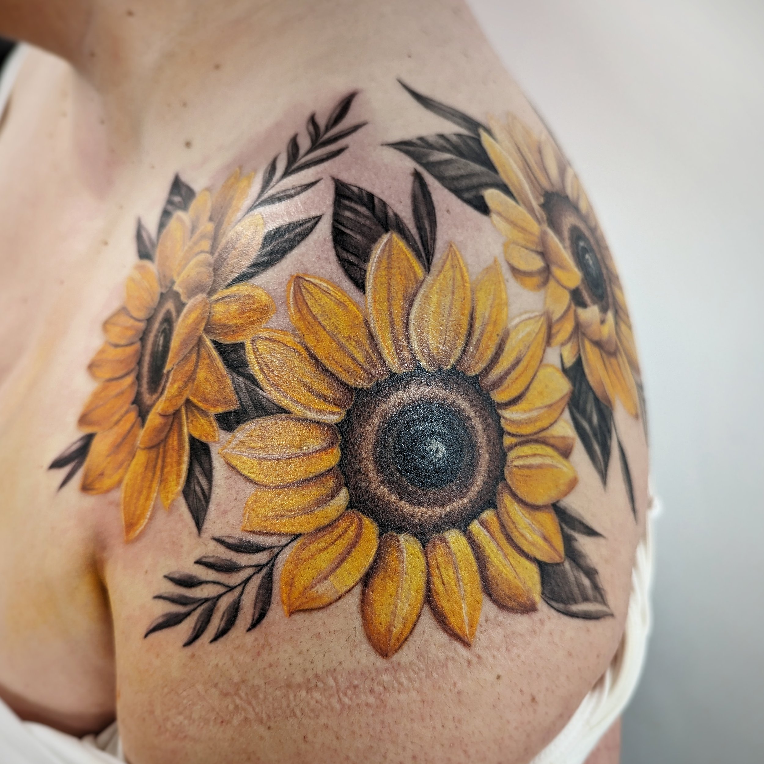 Close-up of a colorful sunflower tattoo on person's skin with detailed black and yellow petals and dark center.