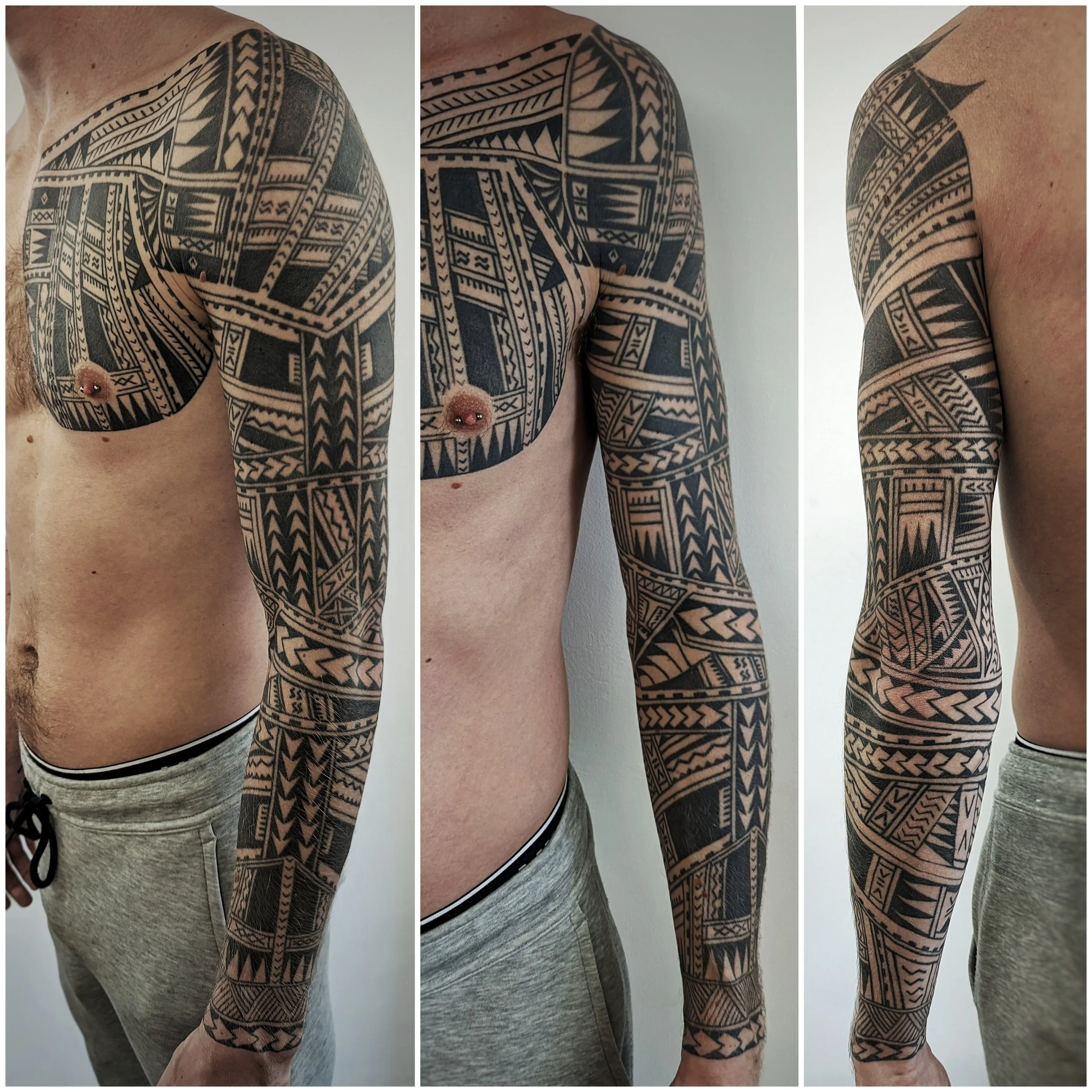 Close-up of a person's upper body with extensive black tribal tattoos covering the shoulder, chest, and arm, featuring geometric patterns and bold lines, wearing gray shorts with black waistband.