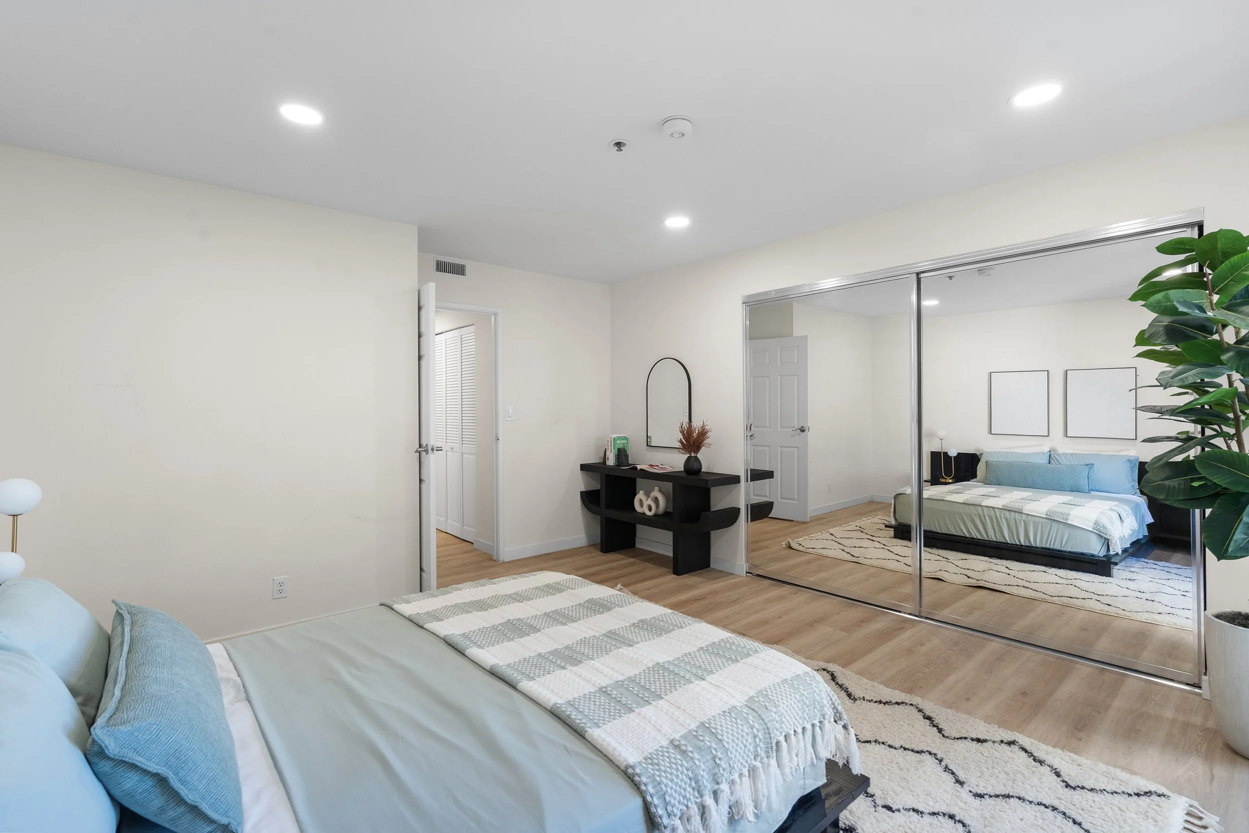 Living room with a bed, pillows, a black dresser, mirror, and a closet with sliding mirror doors.