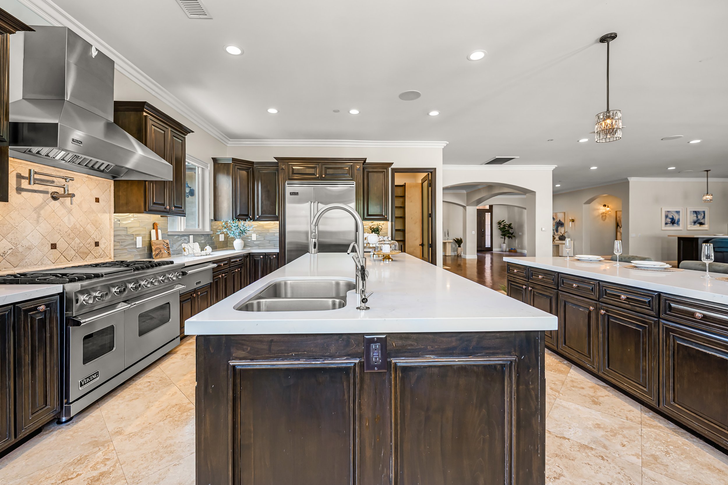 Modern kitchen with dark wooden cabinets, stainless steel appliances, marble countertops, and a kitchen island with a double sink.