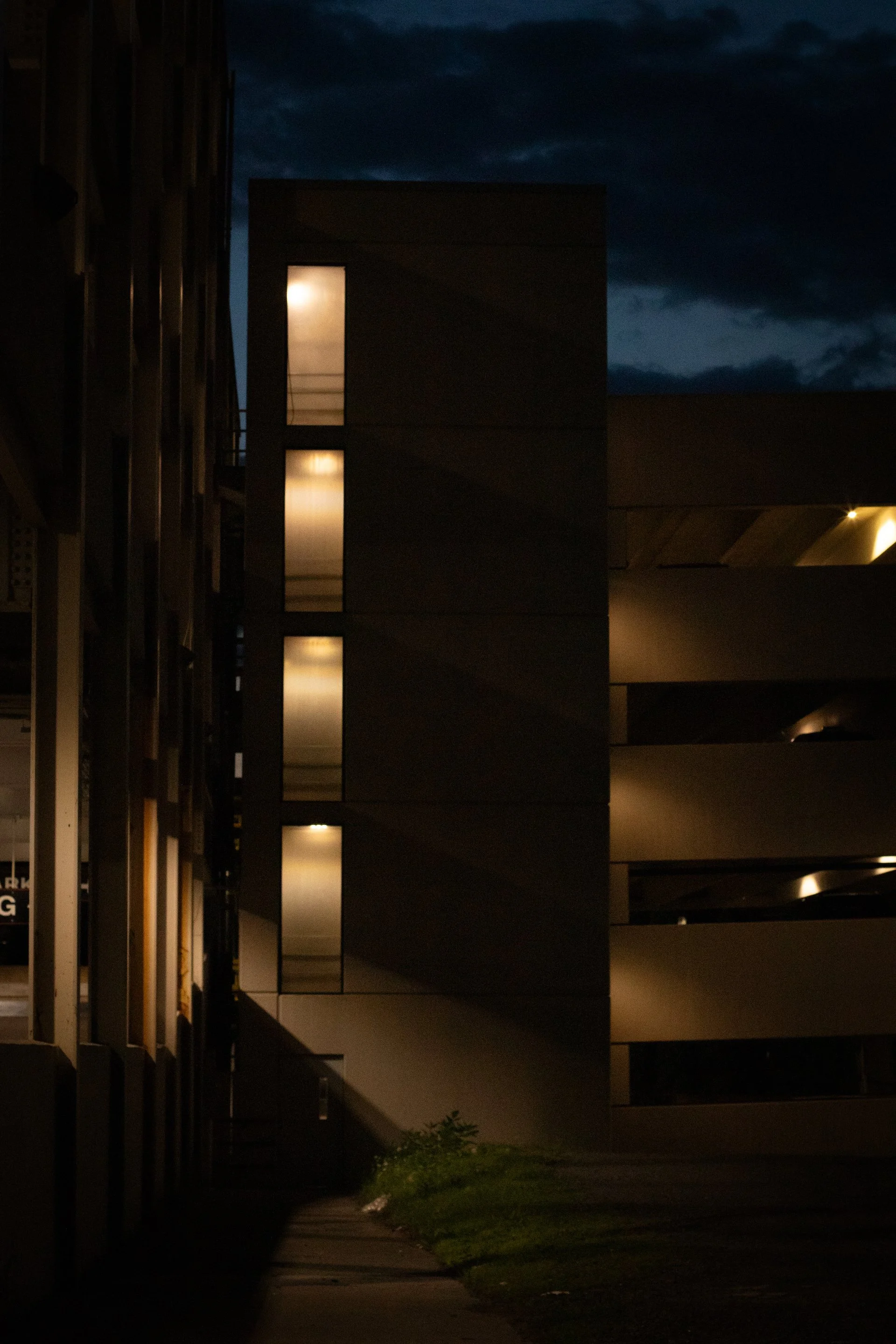 Nighttime view of a modern parking garage with illuminated windows and a dark sky.