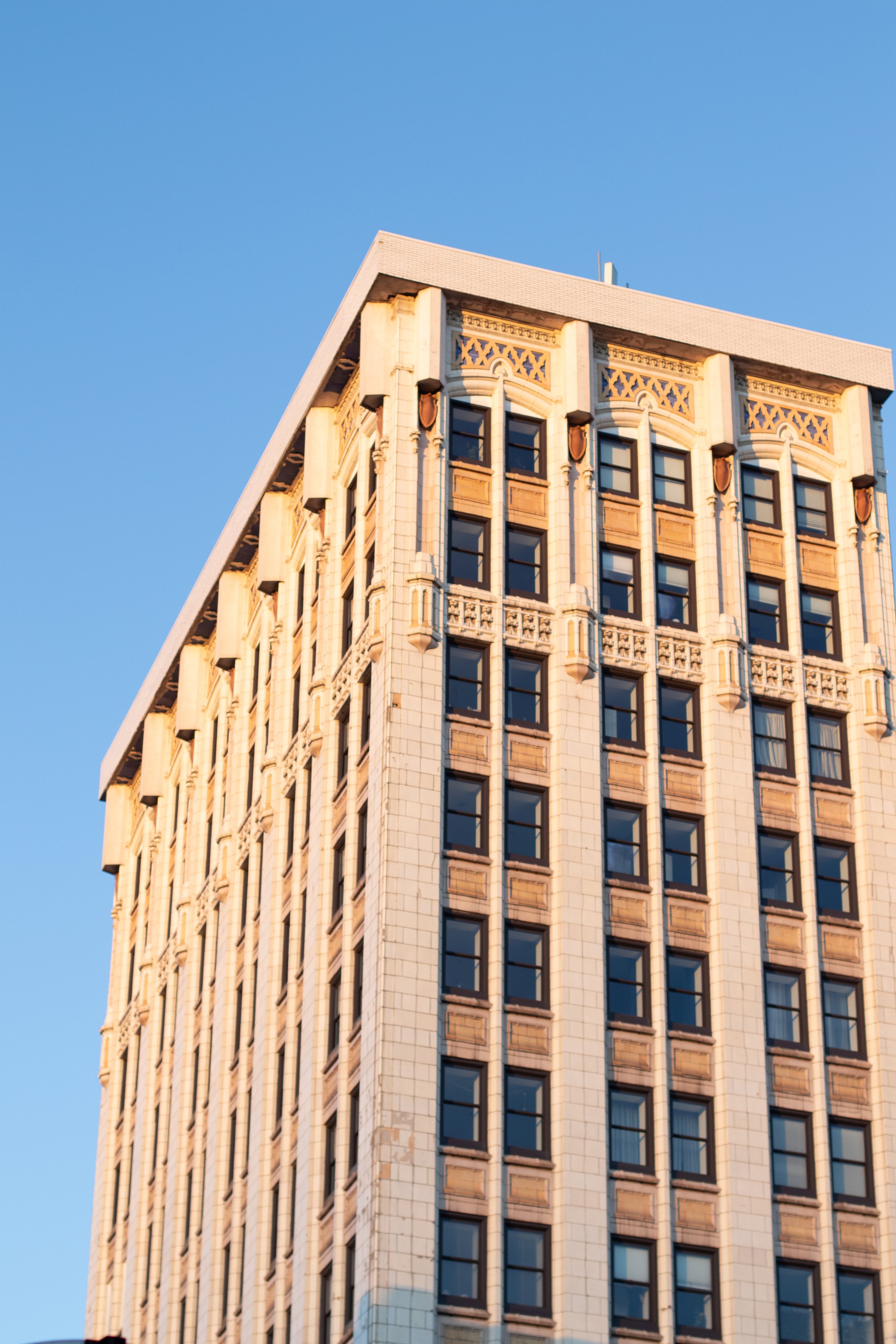 A tall beige skyscraper with ornate architectural details against a clear blue sky.