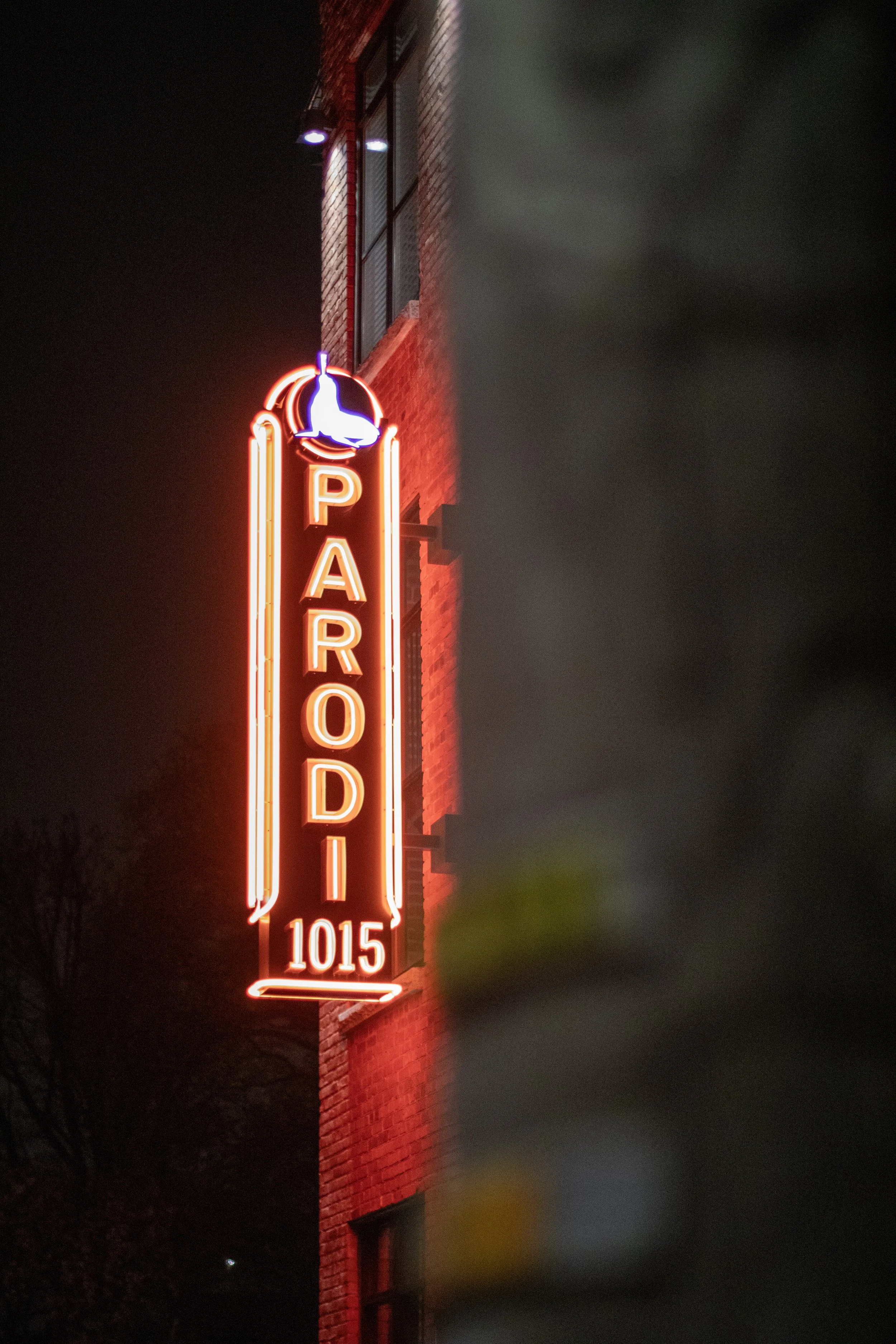 Neon sign for Parodi with the address 1015 on a brick building at night.