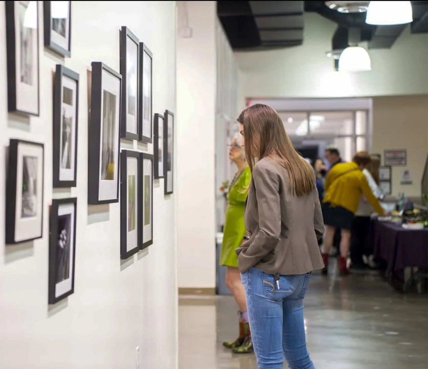 People viewing framed photographs or artwork on a gallery wall at an art exhibit or gallery.