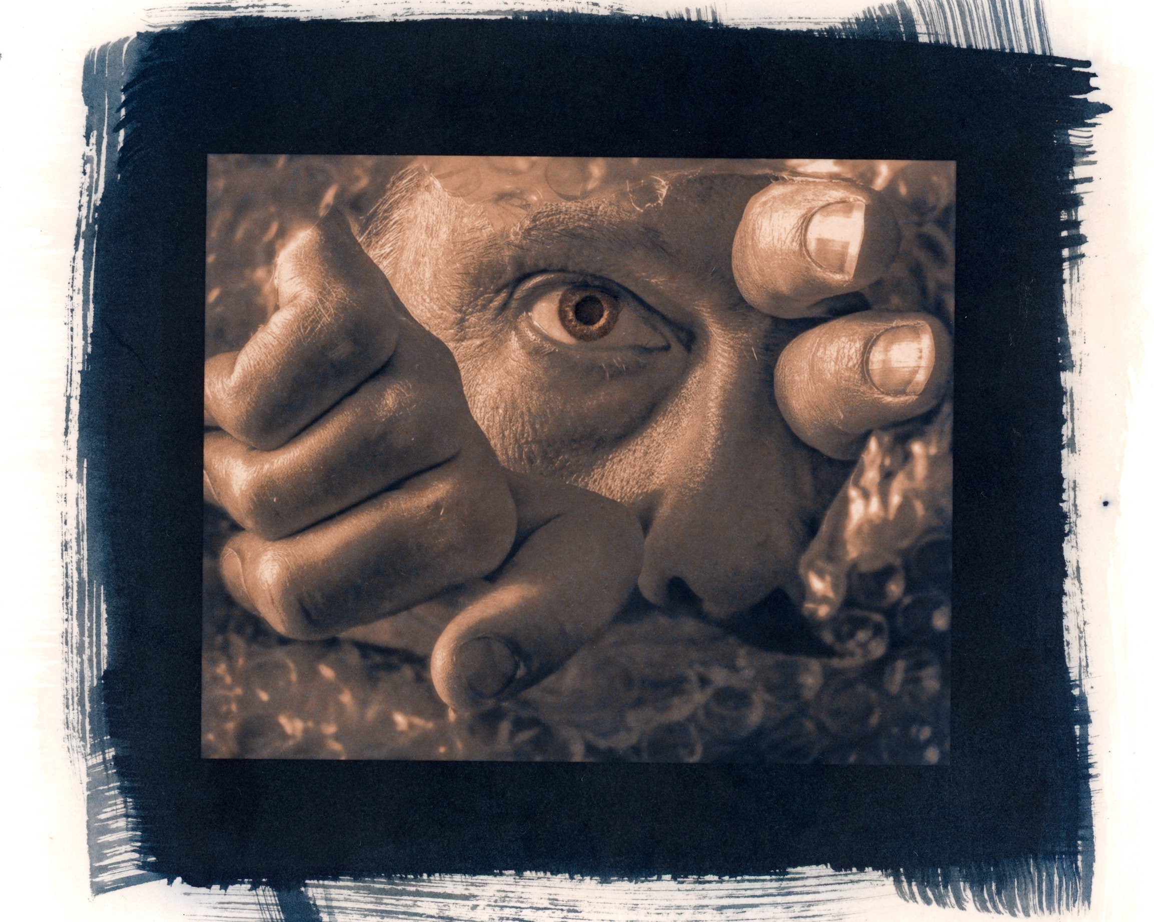 Close-up of a printed photograph showing a person's eye and hand, framed with black paintbrush strokes on paper.
