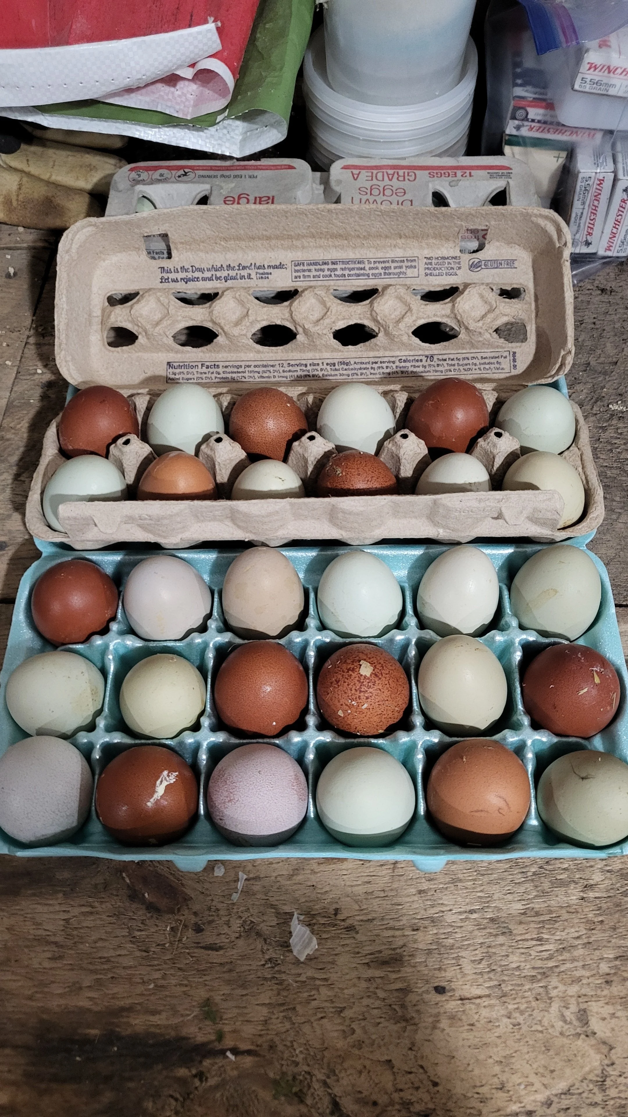 Three trays of eggs in different colors, including white, brown, and speckled. The trays are stacked on a wooden surface surrounded by various household items.