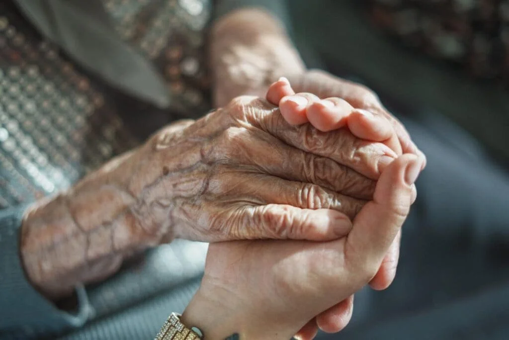 A young person holding an elderly person's wrinkled hand.