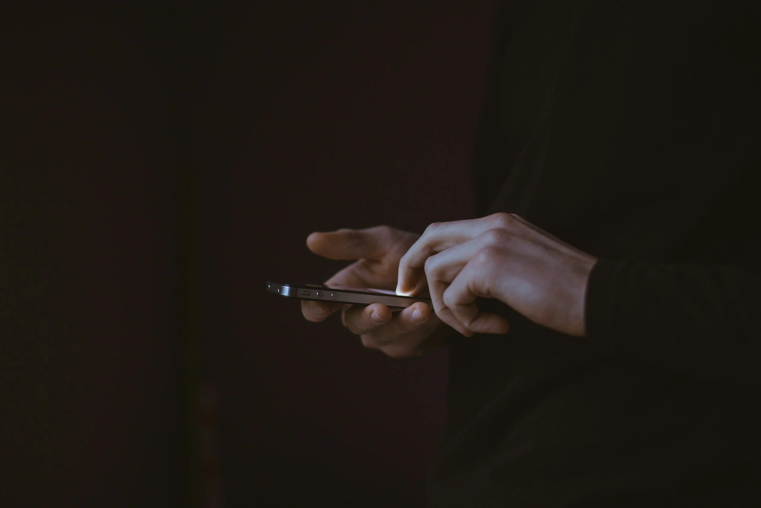 Close-up of hands holding and using a smartphone in a dark environment.
