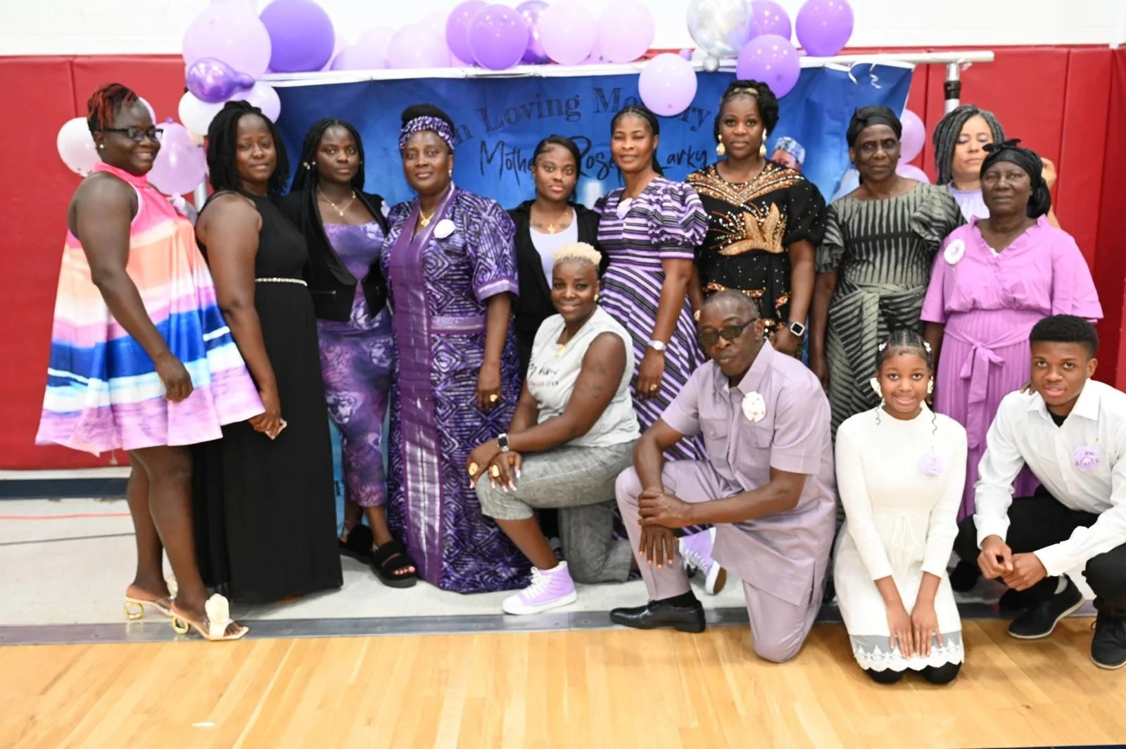 Group of women and children at a celebration, with balloons and a blue banner in the background.