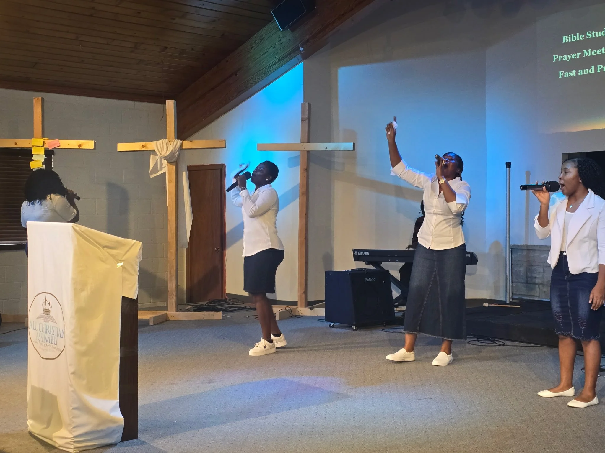 People participating in a church service or religious event, singing and praying, with a cross banner and a lectern with a church logo.