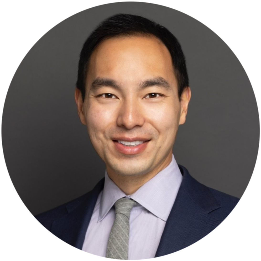 Professional headshot of a man in a suit and tie smiling against a gray background.