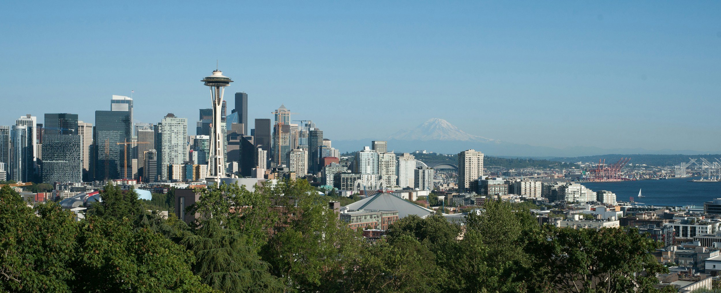 View of downtown Seattle with the Space Needle, skyscrapers, Mount Rainier in the background, and a clear blue sky.