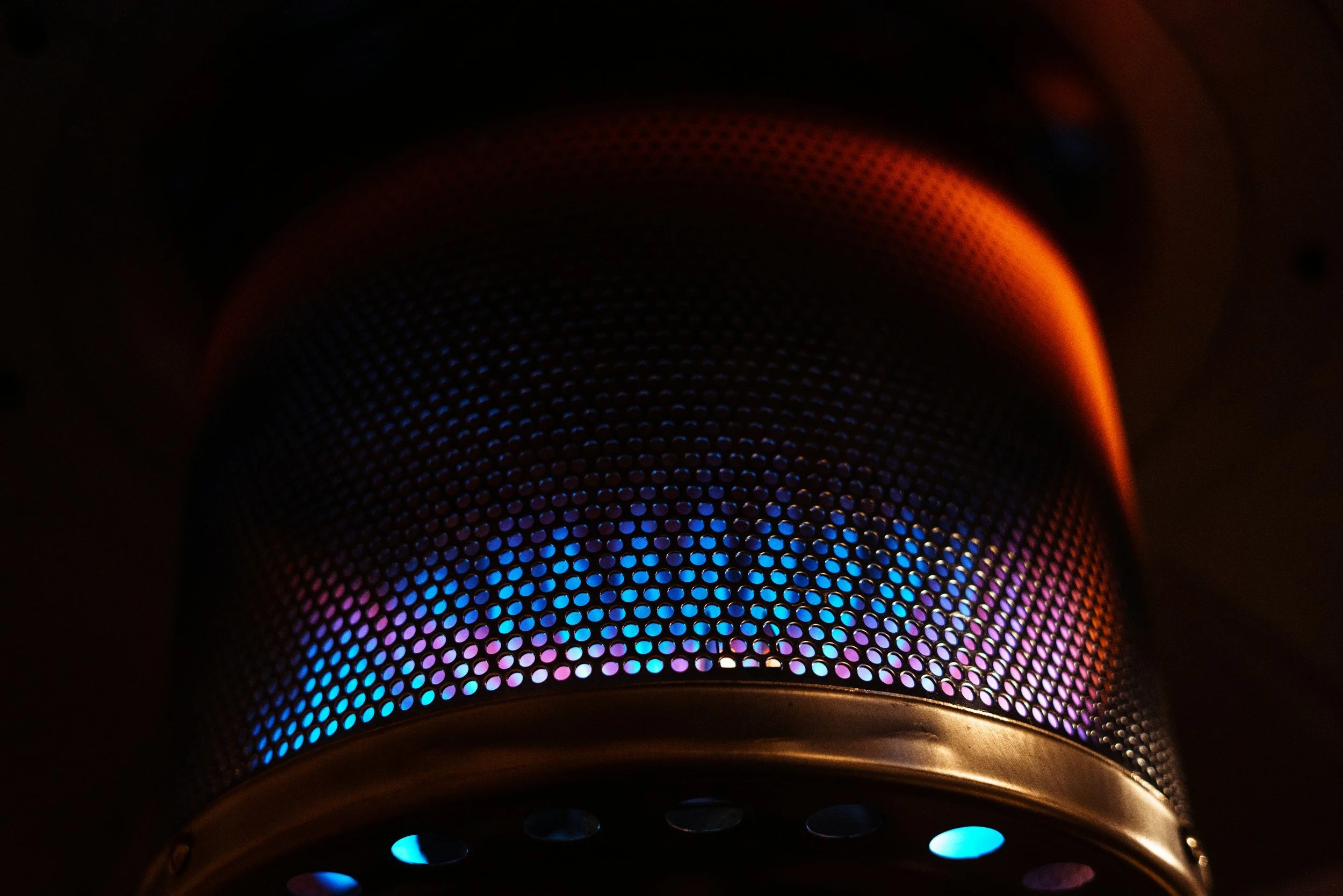 Close-up of a speaker cone with blue and orange LED lights behind a perforated metal grille.