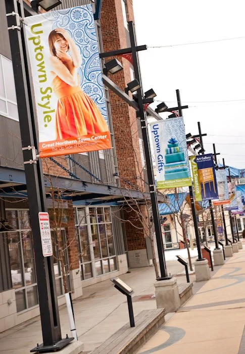 Downtown street with banners promoting Uptown North, featuring a woman in an orange skirt, and other banners for Uptown Arts and other local attractions.