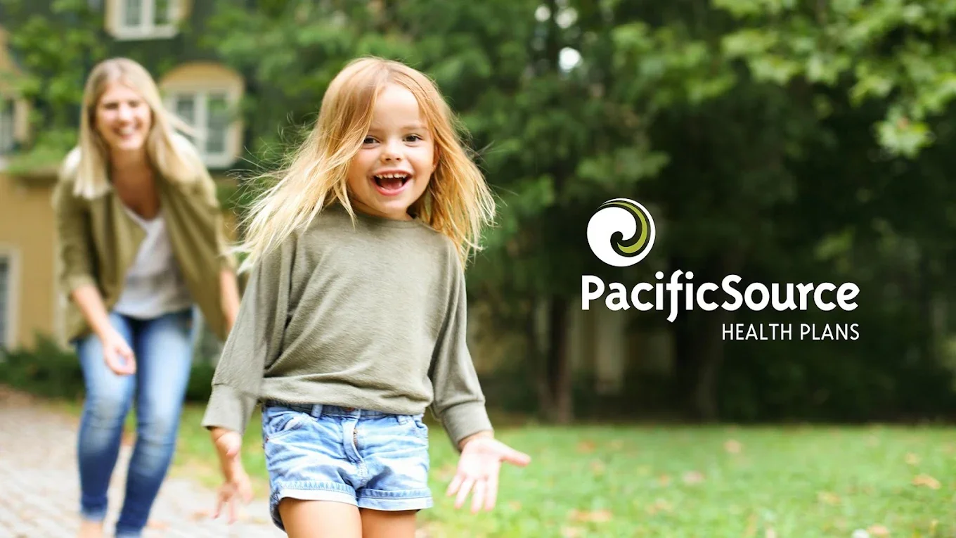 Young girl with red hair smiling and playing outside with a woman, possibly her mother, in a park or yard with green trees and grass.