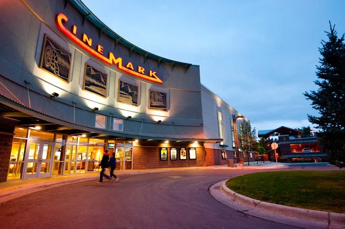 Cinemark movie theater exterior at dusk with illuminated signage and a few pedestrians walking.