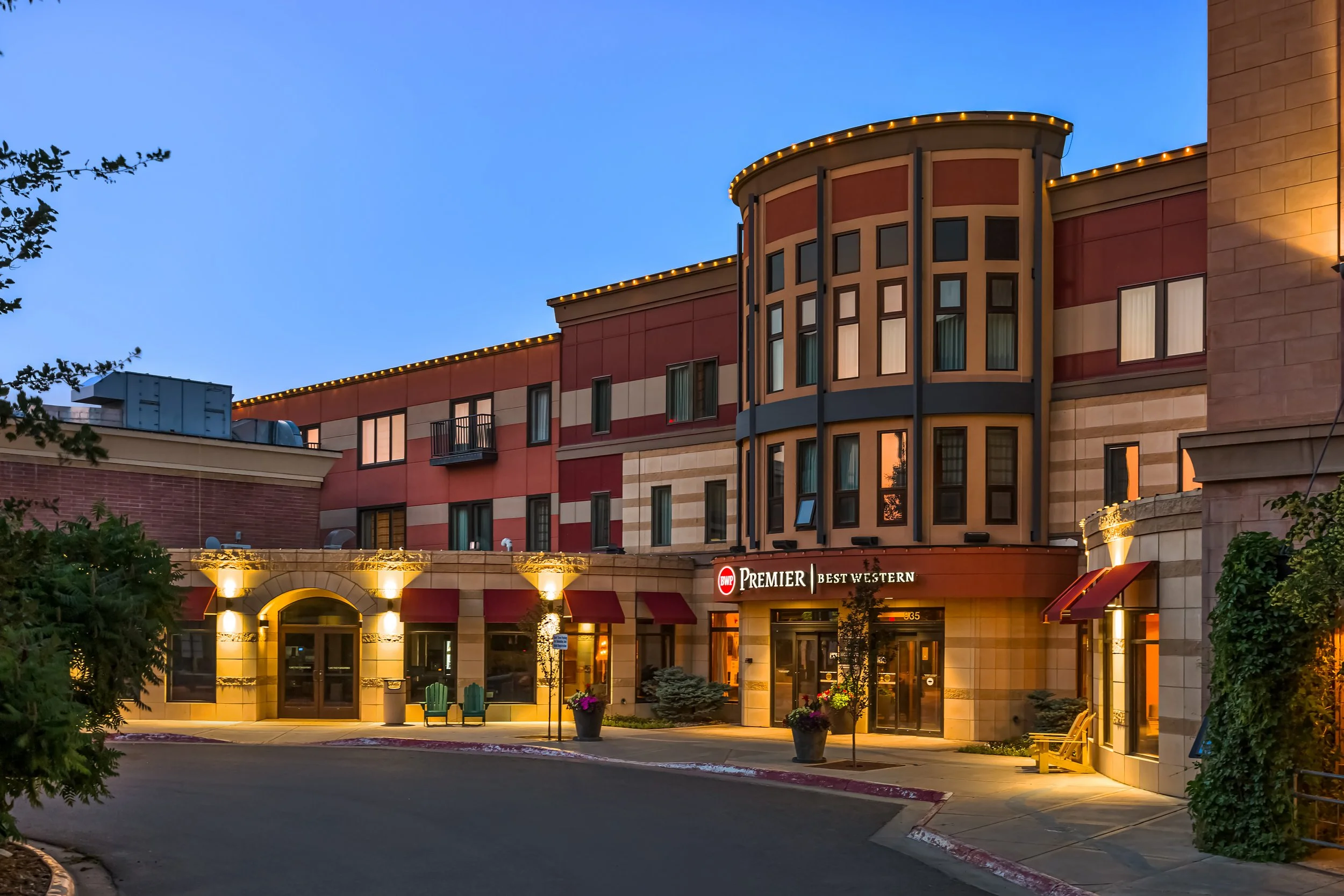 Exterior of a Best Western Premier hotel at dusk, with decorative lights, potted plants, and a front entrance.