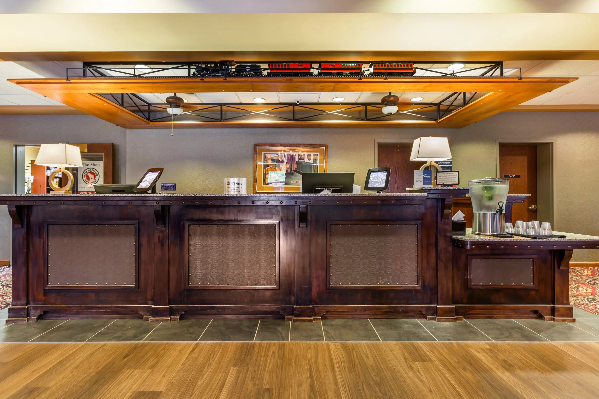 Front desk of a hotel with dark wood finish, lamps, monitors, and a glass of water with lemon and mint on a tray to the right.