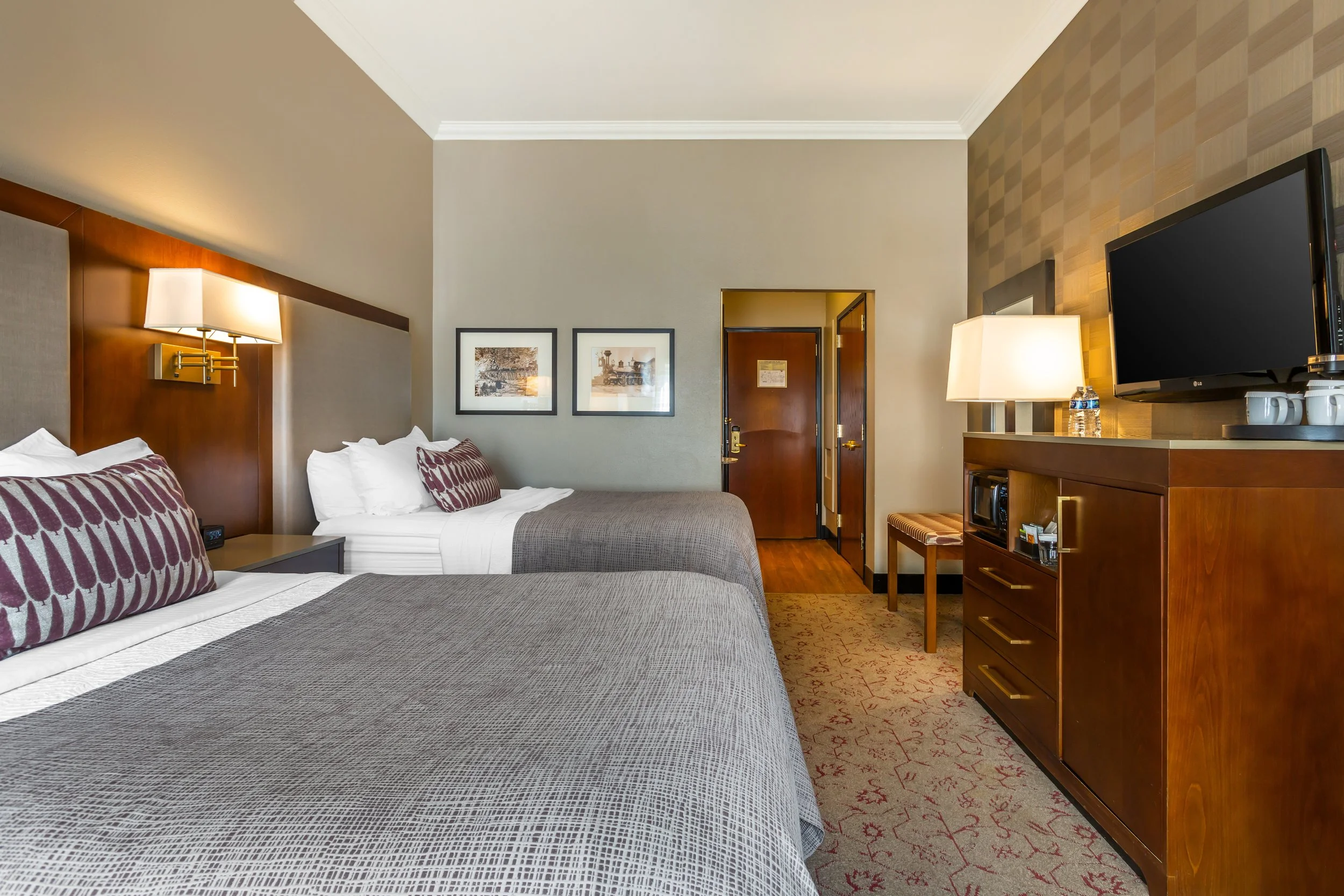 Hotel room with two beds, a dresser with a TV and lamp, and framed pictures on the wall.