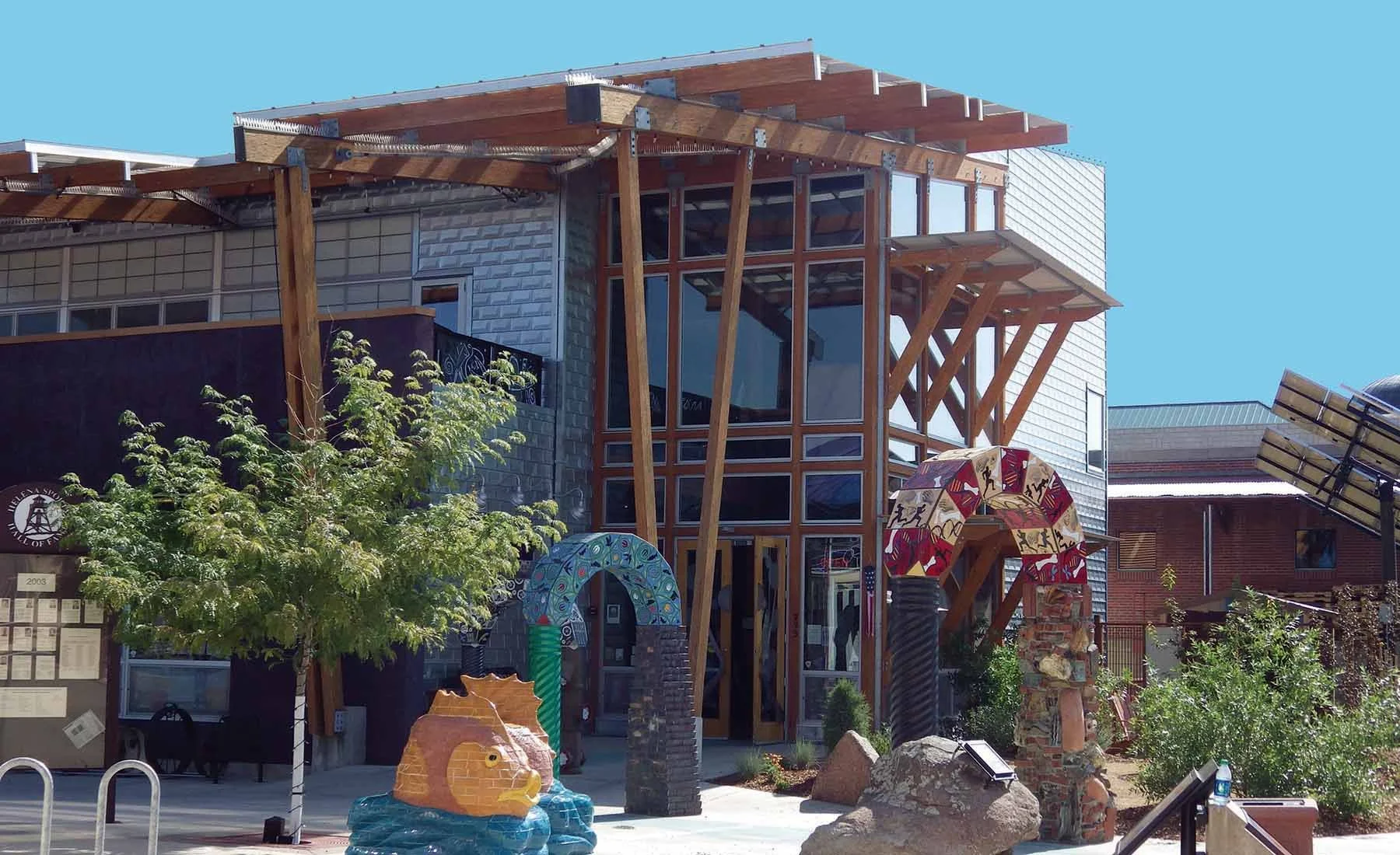 Modern building with large glass windows and wood accents, colorful sculptures, greenery, and outdoor decorations
