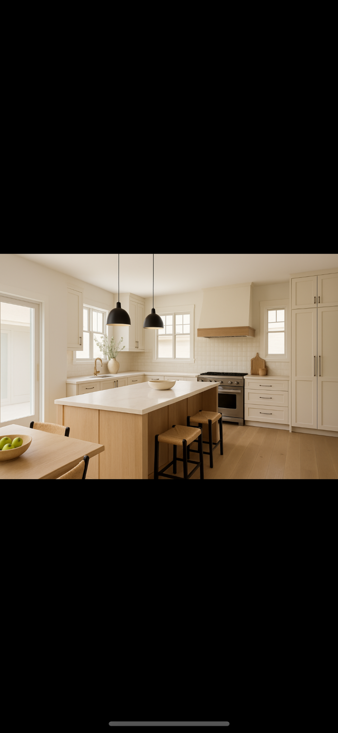 Bright, modern kitchen with white cabinetry, a large central island with a white countertop, three black pendant lights hanging from the ceiling, and light wood flooring. There are two windows above the kitchen sink, a sliding glass door on the left, and a small table with a bowl of green apples in the foreground.