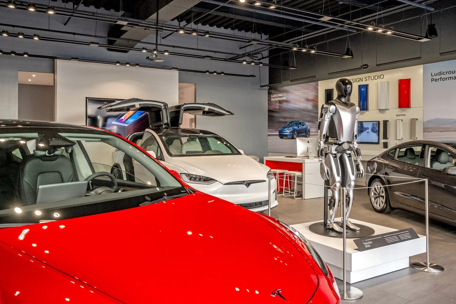 Interior of a Tesla showroom displaying various electric cars, a robot statue, and design elements.