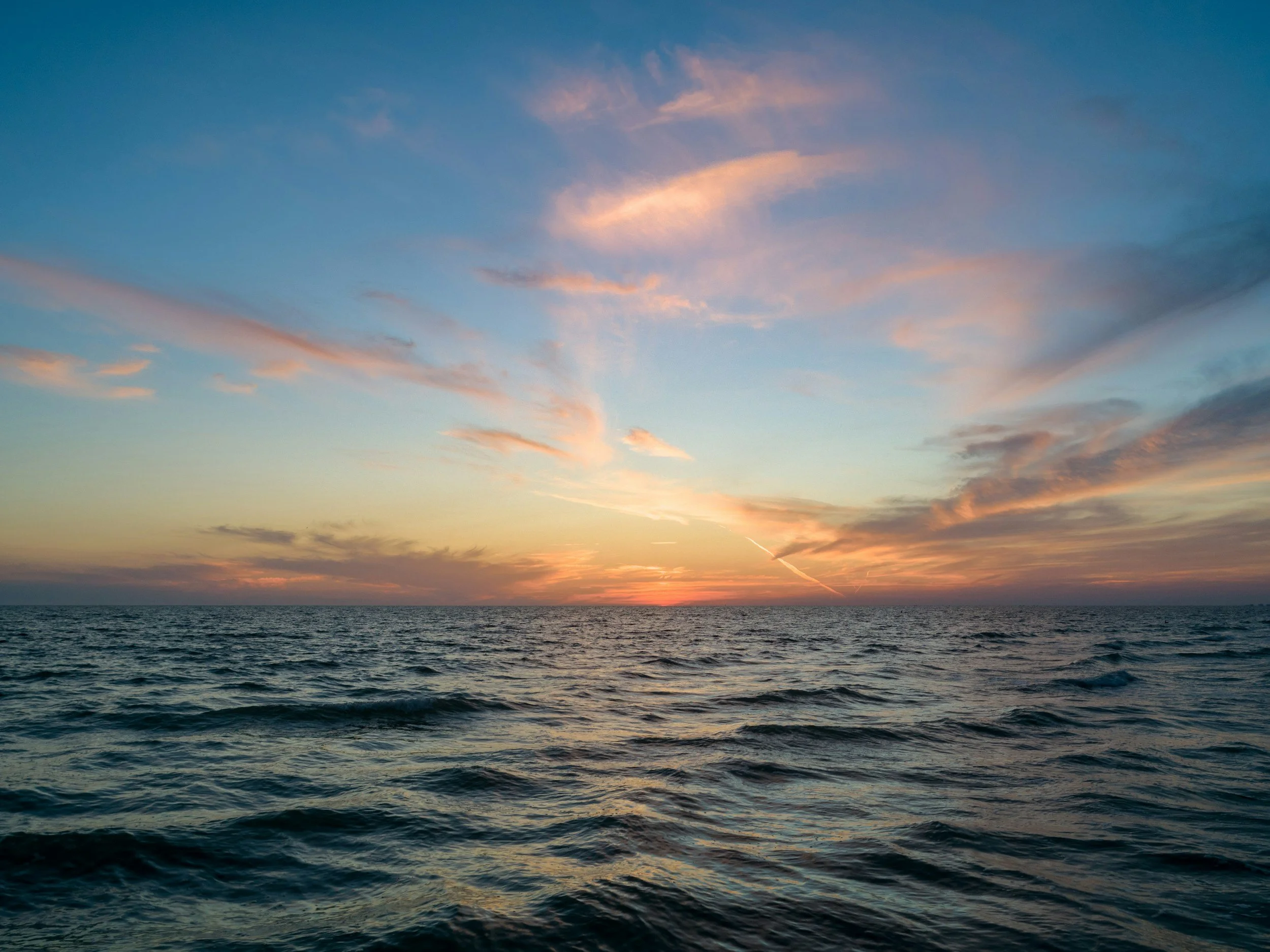 Ocean sunset with colorful clouds in the sky and calm water in the foreground.