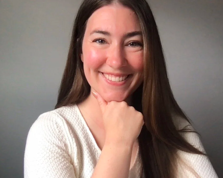 The Founder and CEO, Kristiana Haiar, smiling and resting her chin on her hand, wearing a white textured shirt, against a plain gray background.